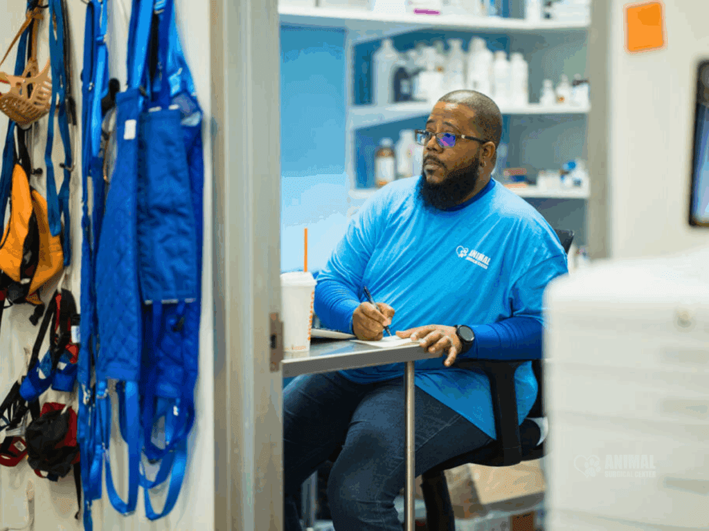A man wearing a blue shirt sits at a desk, taking notes in a well-organized workspace filled with various supplies, showcasing a professional environment.